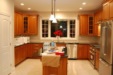 Mid-sized traditional u-shaped kitchen in New York with an undermount sink, raised-panel cabinets, medium wood cabinets, stainless steel appliances, with island, beige floor and black benchtop.