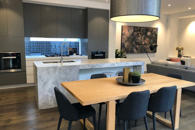 Photo of a galley open plan kitchen in Melbourne with an undermount sink, grey cabinets, marble benchtops, glass sheet splashback, medium hardwood floors, with island, grey floor and grey benchtop.
