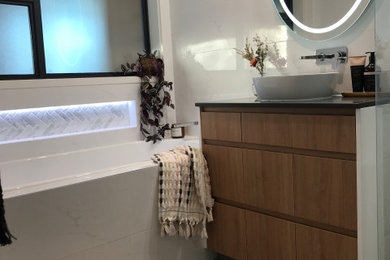 This is an example of a mid-sized contemporary bathroom in Canberra - Queanbeyan with medium wood cabinets, a drop-in tub, white tile, ceramic tile, a vessel sink, engineered quartz benchtops, black benchtops, a single vanity and a floating vanity.