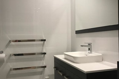 Inspiration for a mid-sized modern master bathroom in Auckland with furniture-like cabinets, brown cabinets, a corner shower, a one-piece toilet, beige tile, ceramic tile, grey walls, ceramic floors, a pedestal sink, wood benchtops, grey floor and a hinged shower door.