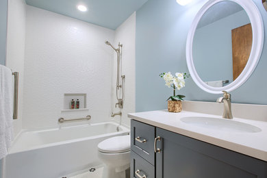 This is an example of a mid-sized transitional 3/4 bathroom in Seattle with shaker cabinets, grey cabinets, an alcove tub, a shower/bathtub combo, a two-piece toilet, white tile, ceramic tile, grey walls, ceramic floors, an undermount sink, solid surface benchtops, white floor, a shower curtain and white benchtops.