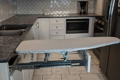 Inspiration for a mid-sized timeless l-shaped ceramic tile and white floor enclosed kitchen remodel in New York with a farmhouse sink, raised-panel cabinets, white cabinets, quartz countertops, white backsplash, subway tile backsplash, black appliances, a peninsula and brown countertops