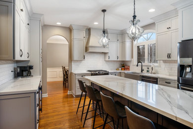 Large transitional u-shaped medium tone wood floor and brown floor eat-in kitchen photo in Cleveland with a farmhouse sink, flat-panel cabinets, white cabinets, quartz countertops, white backsplash, subway tile backsplash, stainless steel appliances, an island and white countertops