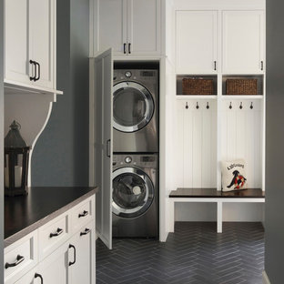 Nautical utility room in Minneapolis with shaker cabinets, white cabinets, wood worktops, grey walls, a stacked washer and dryer and black floors.
