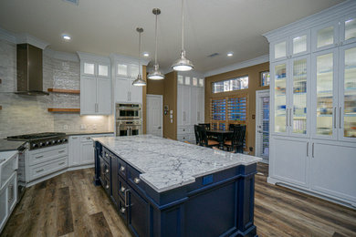 Eat-in kitchen - large craftsman u-shaped medium tone wood floor, brown floor and vaulted ceiling eat-in kitchen idea in Houston with shaker cabinets, white cabinets, granite countertops, gray backsplash, subway tile backsplash, stainless steel appliances, an island, gray countertops and a farmhouse sink