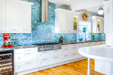 Photo of a mid-sized beach style galley kitchen in San Francisco with a single-bowl sink, shaker cabinets, white cabinets, granite benchtops, blue splashback, mosaic tile splashback, stainless steel appliances, light hardwood floors and a peninsula.
