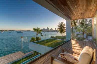 Design ideas for a mid-sized contemporary balcony in Miami with a roof extension and glass railing.