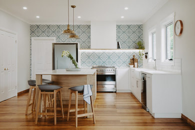 Kitchen in Hobart with a farmhouse sink, white cabinets, granite benchtops, multi-coloured splashback, cement tile splashback, stainless steel appliances, light hardwood floors and with island.
