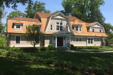 Inspiration for a large timeless beige two-story wood house exterior remodel in New York with a clipped gable roof and a shingle roof