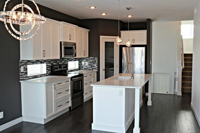 Example of a mid-sized minimalist l-shaped dark wood floor eat-in kitchen design in Calgary with a double-bowl sink, recessed-panel cabinets, white cabinets, granite countertops, gray backsplash, mosaic tile backsplash, stainless steel appliances and an island