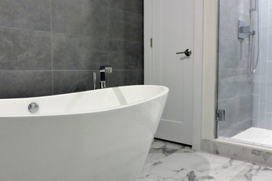 Minimalist master gray tile and porcelain tile porcelain tile and multicolored floor freestanding bathtub photo in Philadelphia with flat-panel cabinets, white cabinets, a two-piece toilet, white walls, a hinged shower door and white countertops