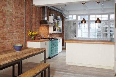 This is an example of a medium sized industrial kitchen/diner in London with a belfast sink, shaker cabinets, white cabinets, wood worktops, stainless steel appliances, medium hardwood flooring and a breakfast bar.