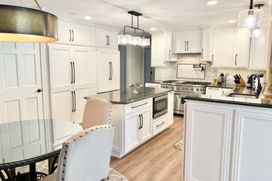 Example of a large classic u-shaped medium tone wood floor and brown floor eat-in kitchen design in Other with a double-bowl sink, recessed-panel cabinets, white cabinets, quartz countertops, white backsplash, porcelain backsplash, paneled appliances, an island and black countertops