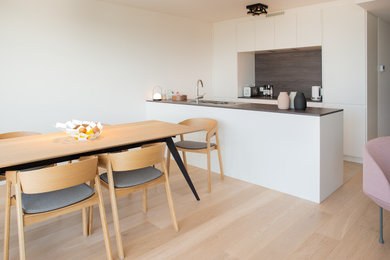 Réalisation d'une cuisine ouverte parallèle design de taille moyenne avec des portes de placard blanches, une crédence marron, une crédence en bois, parquet clair, îlot, un sol beige et plan de travail noir.