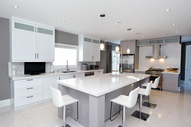 Kitchen pantry - mid-sized transitional l-shaped porcelain tile kitchen pantry idea in Toronto with a double-bowl sink, shaker cabinets, white cabinets, quartz countertops, white backsplash, stone slab backsplash, stainless steel appliances and an island