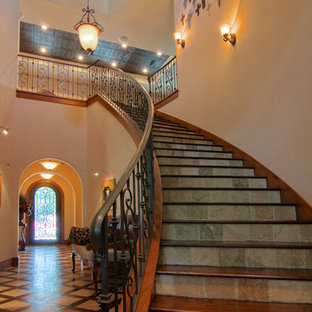 Ejemplo de escalera curva, mediterránea, grande, con escalones de madera, contrahuellas de pizarra y barandilla de metal