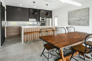 Inspiration for a large modern single-wall concrete floor and gray floor open concept kitchen remodel in Phoenix with an undermount sink, flat-panel cabinets, black cabinets, marble countertops, white backsplash, stainless steel appliances, an island and white countertops