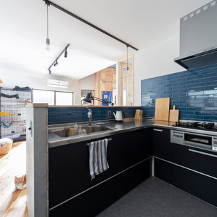 Modelo de cocina en L, urbana, abierta, con fregadero bajoencimera, armarios con rebordes decorativos, puertas de armario negras, encimera de acero inoxidable, salpicadero de azulejos tipo metro, electrodomésticos de acero inoxidable, suelo de baldosas de cerámica, una isla, suelo gris y papel pintado