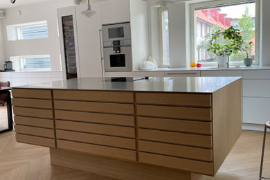 Bild på ett mellanstort skandinaviskt linjärt kök och matrum, med en enkel diskho, luckor med lamellpanel, skåp i ljust trä, bänkskiva i rostfritt stål, integrerade vitvaror, ljust trägolv och en köksö