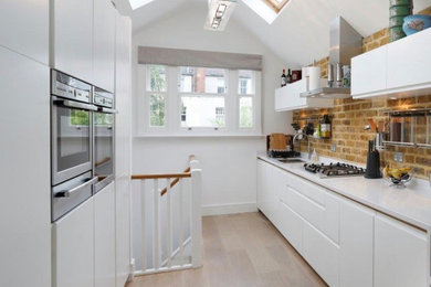 This is an example of a mid-sized scandinavian galley eat-in kitchen in London with flat-panel cabinets, white cabinets, quartzite benchtops, brick splashback, stainless steel appliances, light hardwood floors and white benchtop.