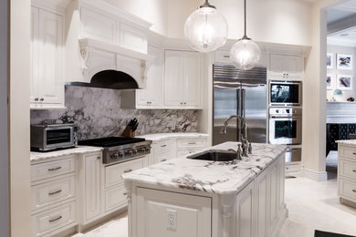 Large transitional u-shaped open plan kitchen in Orlando with multiple islands, an undermount sink, raised-panel cabinets, white cabinets, marble benchtops, grey splashback, marble splashback, stainless steel appliances, white floor and limestone floors.