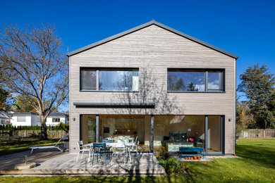 Esempio della villa grigia contemporanea a due piani con rivestimento in legno, tetto a capanna, copertura in tegole, tetto grigio e pannelli sovrapposti