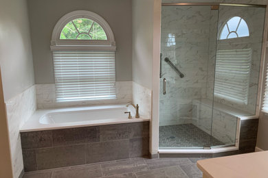 Пример оригинального дизайна: большая главная ванная комната в стиле неоклассика (современная классика) с фасадами с утопленной филенкой, белыми фасадами, полновстраиваемой ванной, душем в нише, раздельным унитазом, белой плиткой, керамогранитной плиткой, серыми стенами, полом из керамогранита, врезной раковиной, столешницей из искусственного кварца, серым полом, душем с распашными дверями, белой столешницей, сиденьем для душа, тумбой под две раковины и встроенной тумбой