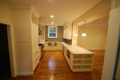 Open concept kitchen - mid-sized traditional u-shaped medium tone wood floor and brown floor open concept kitchen idea in Philadelphia with a farmhouse sink, shaker cabinets, white cabinets, gray backsplash, stainless steel appliances and no island