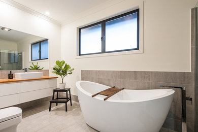 Large contemporary master bathroom in Brisbane with white cabinets, a freestanding tub, a curbless shower, white walls, a vessel sink, wood benchtops, grey floor, recessed-panel cabinets, a two-piece toilet, brown tile, ceramic tile, concrete floors, an open shower and white benchtops.