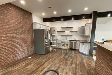Inspiration for a mid-sized industrial u-shaped ceramic tile, brown floor and exposed beam eat-in kitchen remodel in Columbus with a farmhouse sink, raised-panel cabinets, distressed cabinets, wood countertops, white backsplash, shiplap backsplash, stainless steel appliances and brown countertops