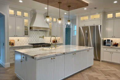 Example of a huge minimalist l-shaped light wood floor, beige floor and wood ceiling open concept kitchen design in Orange County with a farmhouse sink, beaded inset cabinets, white cabinets, white backsplash, marble backsplash, stainless steel appliances, an island and white countertops