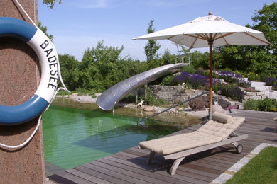 Großer Mediterraner Schwimmteich neben dem Haus in individueller Form mit Wasserrutsche und Natursteinplatten in Nürnberg
