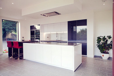 Medium sized modern single-wall open plan kitchen with flat-panel cabinets, white cabinets, an island, quartz worktops and integrated appliances.