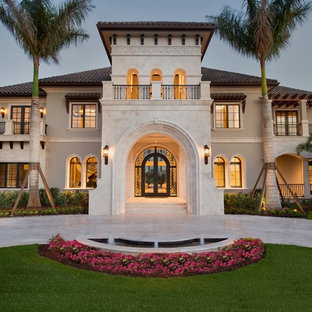 Photo of an expansive mediterranean two-storey stucco beige house exterior in Miami with a hip roof and a tile roof.