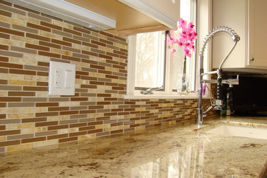 Example of a transitional eat-in kitchen design in New York with recessed-panel cabinets, granite countertops, beige backsplash, glass tile backsplash and stainless steel appliances