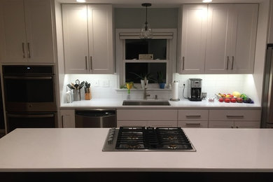 Small transitional single-wall eat-in kitchen photo in New York with an undermount sink, shaker cabinets, white cabinets, solid surface countertops, white backsplash, subway tile backsplash, stainless steel appliances, an island and white countertops