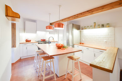 Foto de cocina mediterránea de tamaño medio con armarios con paneles con relieve, puertas de armario blancas, encimera de madera, salpicadero blanco, salpicadero de azulejos tipo metro, electrodomésticos de acero inoxidable, una isla y suelo rojo