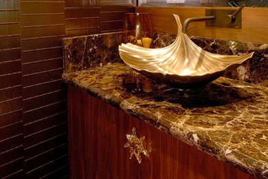 Inspiration for a tropical brown tile and stone tile marble floor powder room remodel in Hawaii with flat-panel cabinets, medium tone wood cabinets, a one-piece toilet, brown walls, a vessel sink and marble countertops