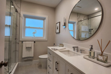 Inspiration for a mid-sized tropical master white tile and porcelain tile porcelain tile, gray floor, single-sink and coffered ceiling bathroom remodel in Miami with recessed-panel cabinets, white cabinets, a one-piece toilet, white walls, an undermount sink, granite countertops, white countertops and a niche