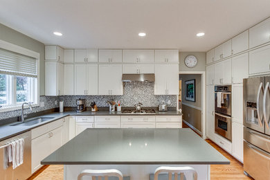Example of a large trendy u-shaped light wood floor and beige floor kitchen design in Other with an undermount sink, shaker cabinets, white cabinets, solid surface countertops, gray backsplash, stone slab backsplash, stainless steel appliances, an island and gray countertops