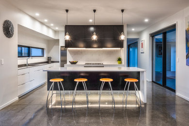 This is an example of a large contemporary l-shaped kitchen pantry in Christchurch with an integrated sink, flat-panel cabinets, white cabinets, quartz benchtops, multi-coloured splashback, stainless steel appliances, concrete floors, with island, grey floor and white benchtop.