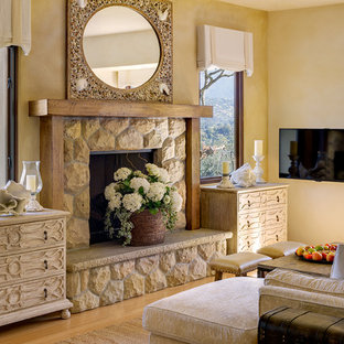 Mittelgroßes Mediterranes Wohnzimmer mit gelber Wandfarbe, Bambusparkett, Kamin, Kaminsims aus Stein und Wand-TV in Santa Barbara