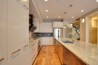 Large minimalist l-shaped medium tone wood floor and brown floor open concept kitchen photo in Calgary with a double-bowl sink, flat-panel cabinets, white cabinets, granite countertops, gray backsplash, stone tile backsplash, stainless steel appliances and an island