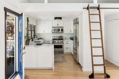 Small beach style u-shaped eat-in kitchen photo in San Francisco with an integrated sink, flat-panel cabinets, white cabinets, white backsplash, stainless steel appliances, no island and white countertops