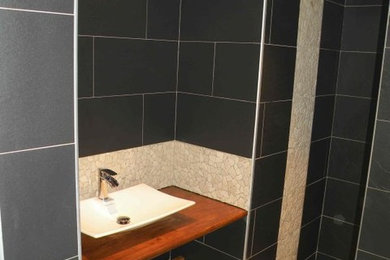 Exemple d'une petite salle de bain principale tendance avec un carrelage noir, des carreaux en allumettes, un mur noir, carreaux de ciment au sol, une grande vasque, un plan de toilette en bois, un sol beige et aucune cabine.