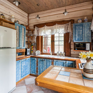 Ejemplo de cocina en U, rural, con fregadero encastrado, armarios con paneles con relieve, puertas de armario azules, península y encimera de azulejos