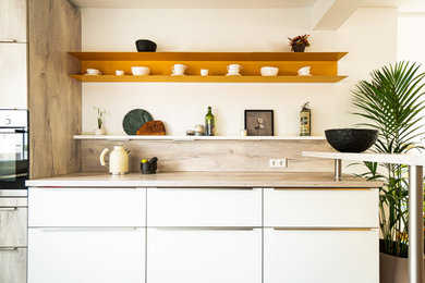 Offene, Zweizeilige, Kleine Moderne Küche ohne Insel mit Glasfronten, weißen Schränken, Laminat-Arbeitsplatte und Elektrogeräten mit Frontblende in Hannover