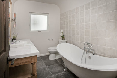 Example of a mid-sized classic kids' beige tile cement tile floor claw-foot bathtub design in Los Angeles with open cabinets, light wood cabinets, a two-piece toilet, beige walls, a drop-in sink and marble countertops