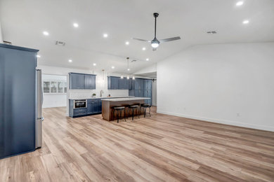 Inspiration for a mid-sized farmhouse vinyl floor and brown floor kitchen remodel in Phoenix with an undermount sink, recessed-panel cabinets, blue cabinets, quartzite countertops, white backsplash, ceramic backsplash, stainless steel appliances, an island and multicolored countertops