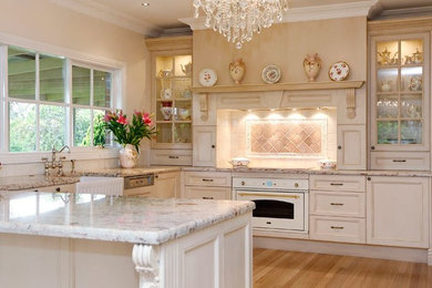 Inspiration for a large traditional u-shaped open plan kitchen in Melbourne with a farmhouse sink, recessed-panel cabinets, white cabinets, marble benchtops, beige splashback, ceramic splashback, white appliances, light hardwood floors and with island.